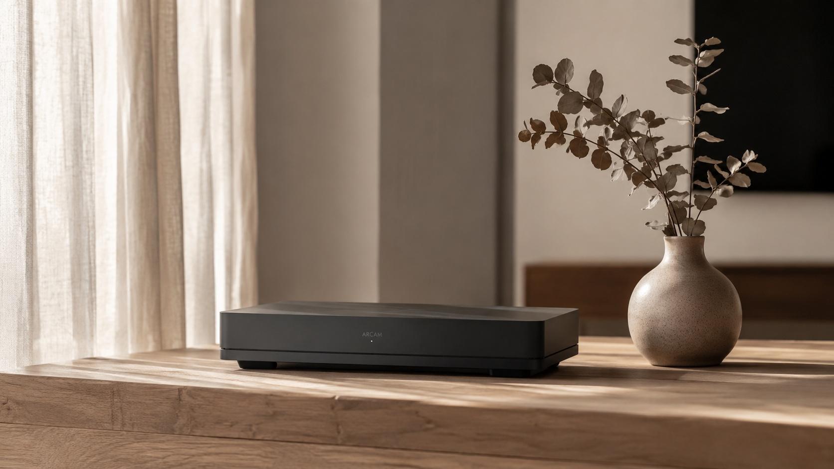A minimalist workspace with a matte black device and a eucalyptus branch in a ceramic vase, illuminated by soft natural sunlight.